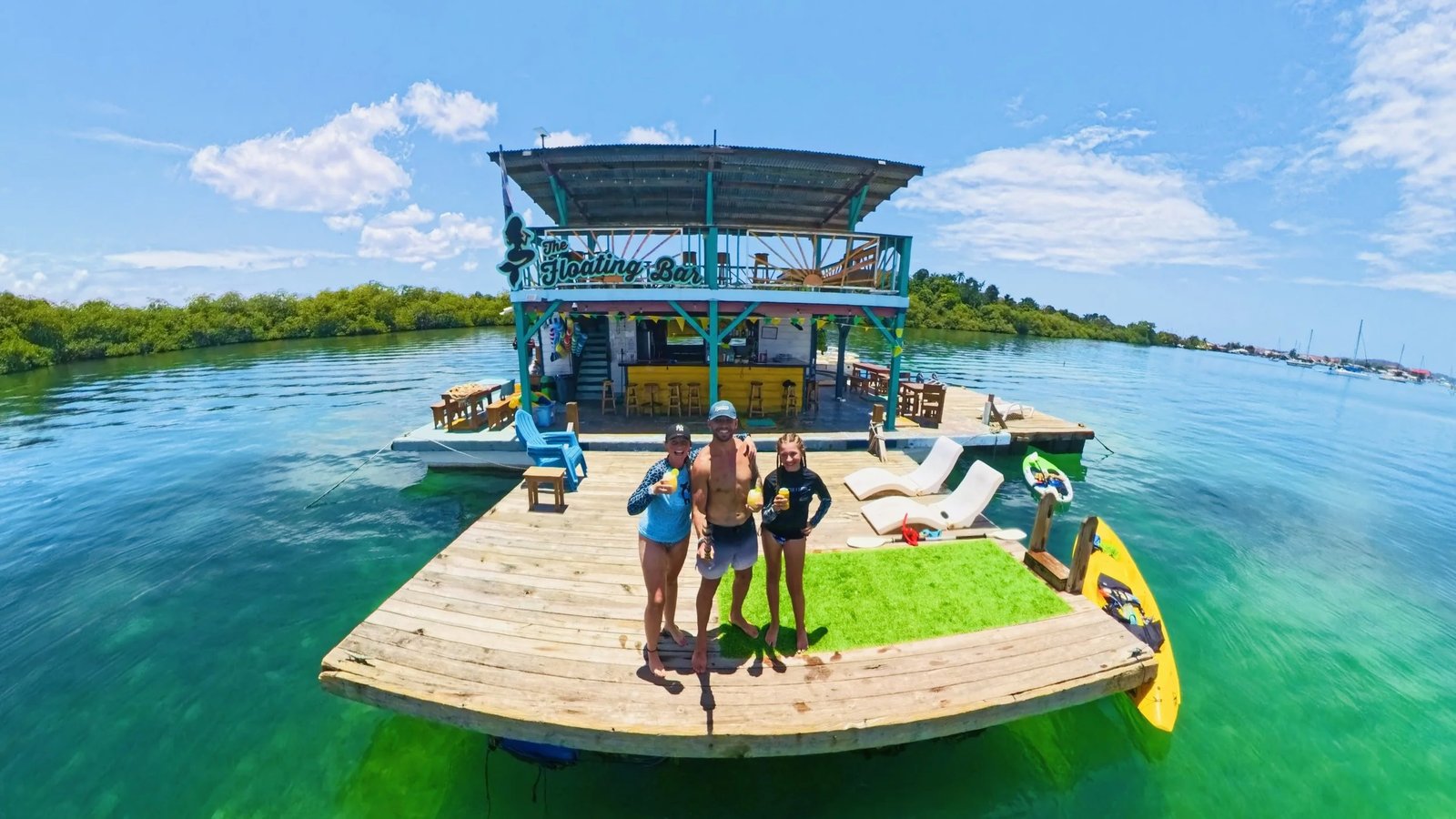 Guests with drinks on the swim deck at The Floating Bar — two decks and the mermaid sign anchored in turquoise water off Isla Colón, Panama